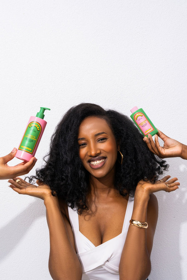 Woman with natural curls smiling while holding Froday leave-in conditioner and hair oil