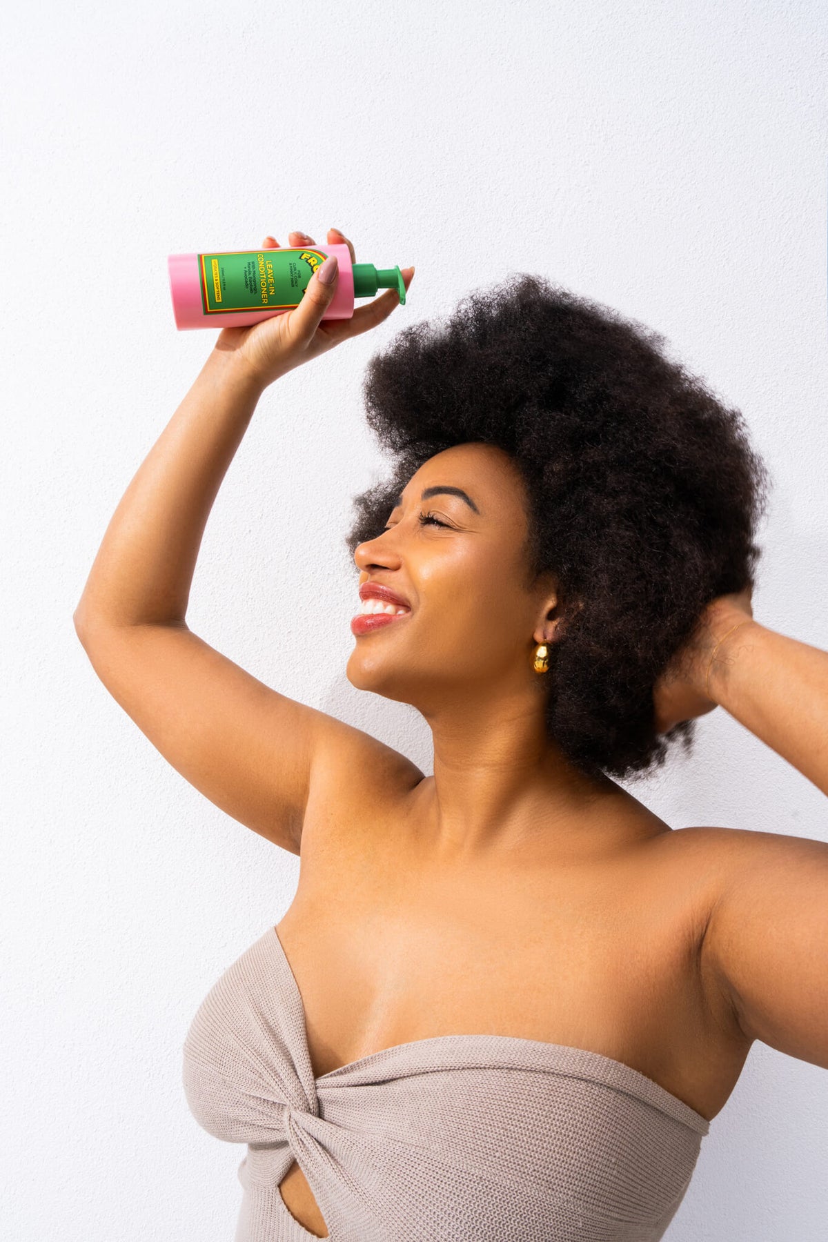 Woman with natural afro holding Froday leave-in conditioner for hydration and volume